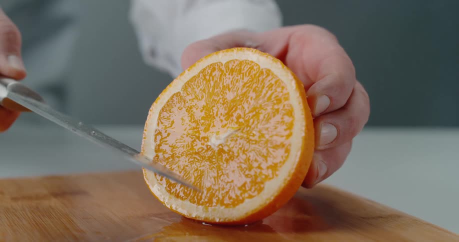 A person with a knife cutting a orange on a cutting board