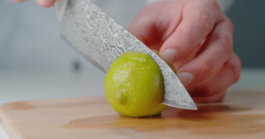A person with a knife cutting a lime on a cutting board