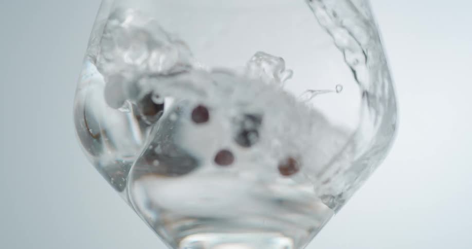 Water pouring over a round ice cube and berries in a wine glass