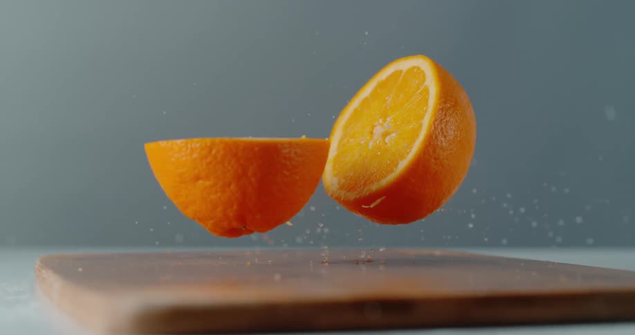 Two pieces of orange falling on a cutting board on a table
