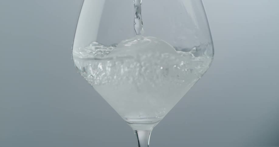 Clear crystal liquid pouring over an ice ball inside a wine glass