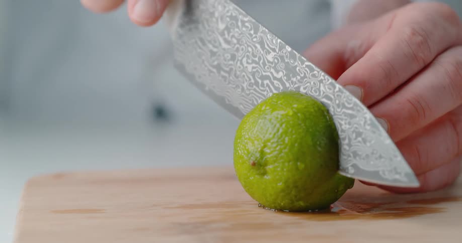 A man uses a large knife with an intricately designed blade to cut a lime in half