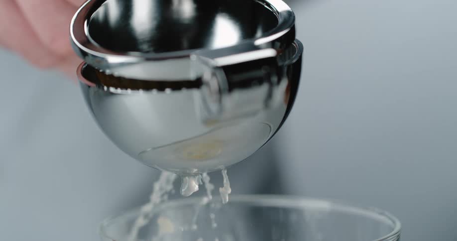 A person squeezing a lemon over a glass using an aluminium lemon squeezer