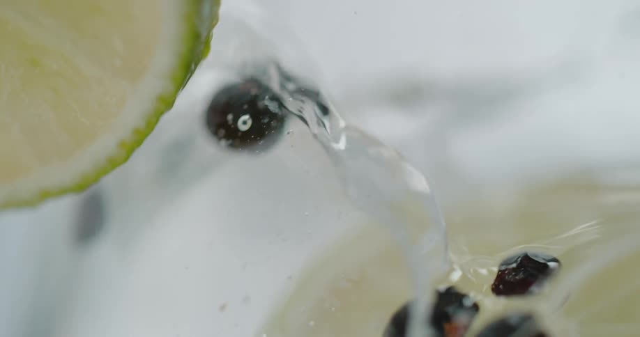 Slice of lemon or lime falling inside a crustal clear beverage inside a glass