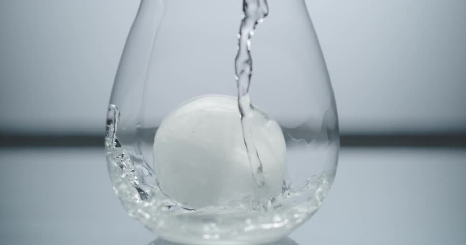 Water pouring over a round ice cube in a glass