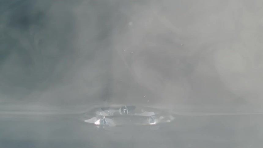 A drop of water splashes up as its dropped from above onto steaming hot water