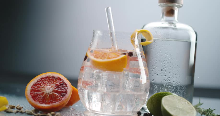 Clear crystal ice cubes falling over orange slices in a cocktail inside a glass or goblet