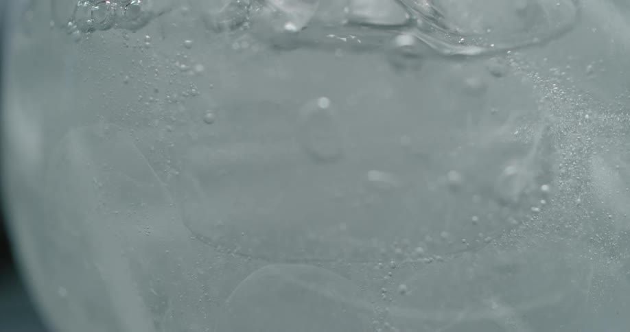 Liquid filling glass with ice inside and bubbles are rising up