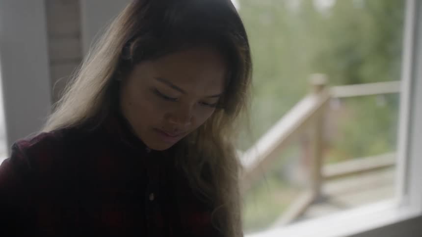 A woman is looking down near the window of a home.'