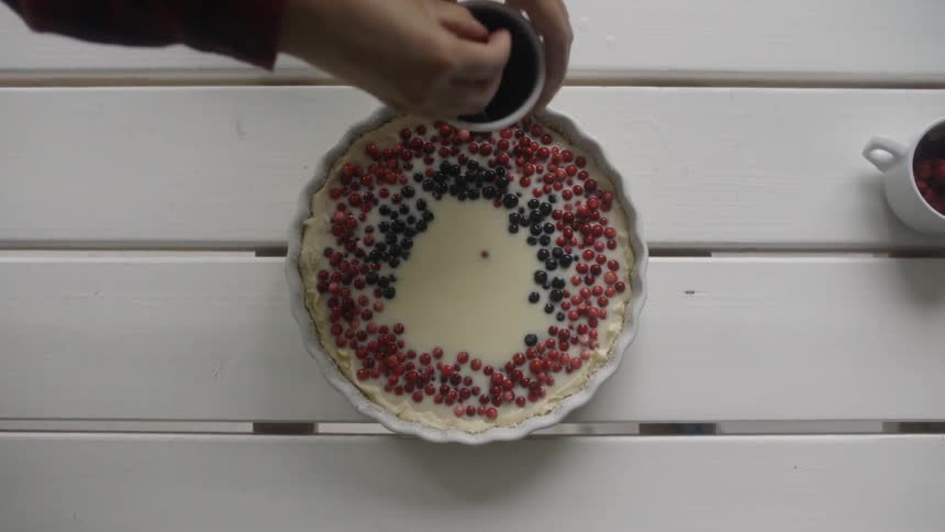 A person puts berries on a custard dessert
