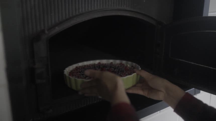 A person opens an oven and places a pie inside to cook