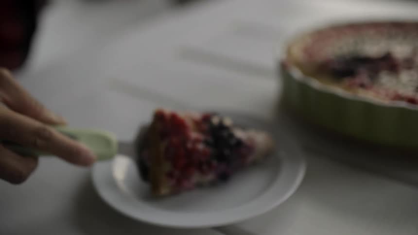 A person slices a piece of dessert and puts it on a plate