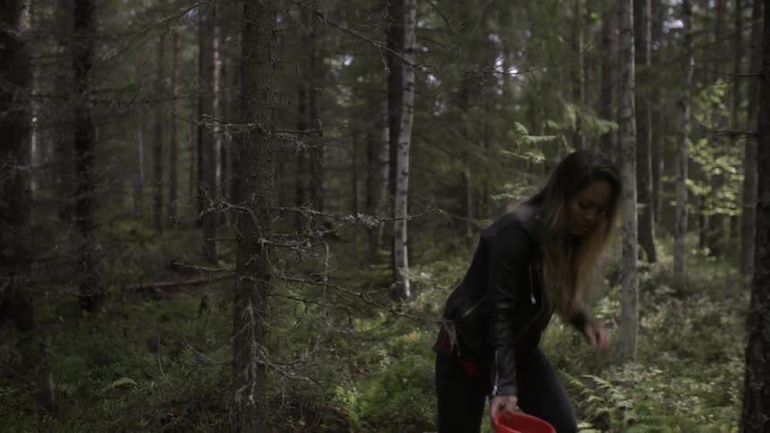 A woman is walking in the woods with a bowl in her hands