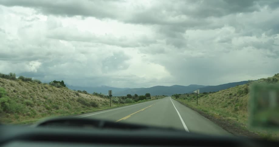 A vehicle driving on a road with signs with a mountain range the sky and clouds in the background