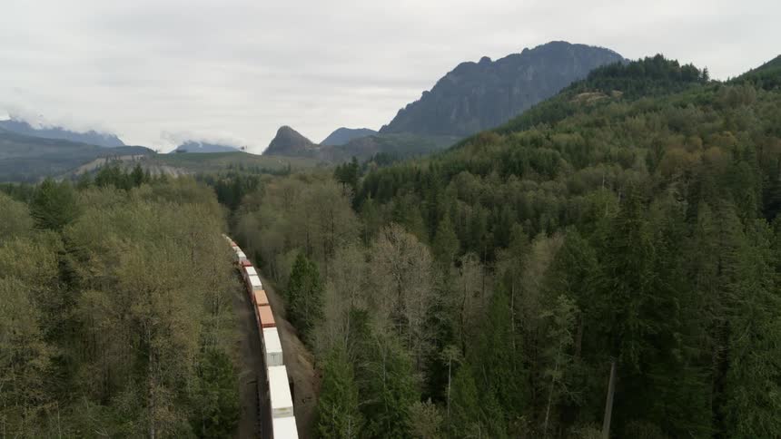 Orbiting traverse over an intermodal freight train traveling through rugged mountains and forest