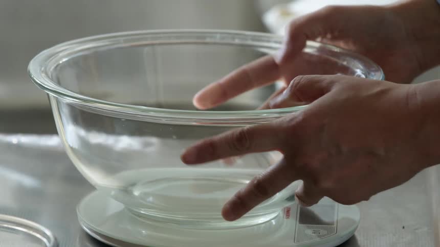A person placing a glass mixing bowl over a scale on the kitchen counter top