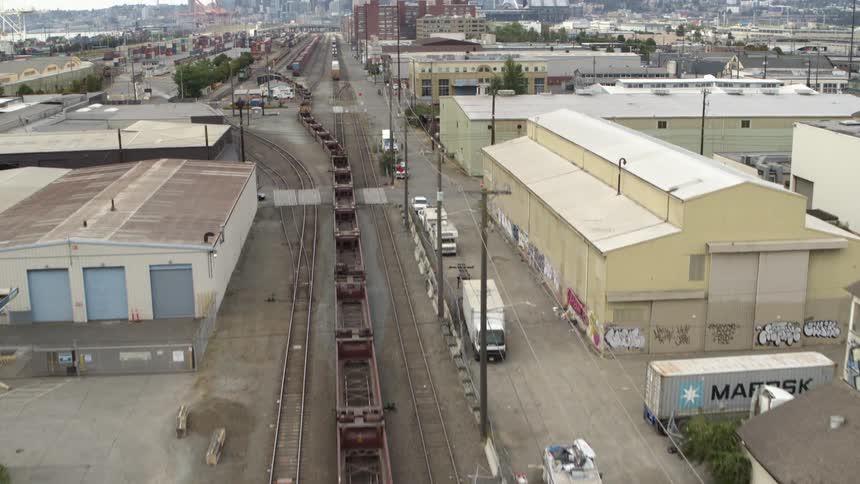Tilt up ascent reveal of empty container cars leaving a staging yard in a gritty urban industrial district
