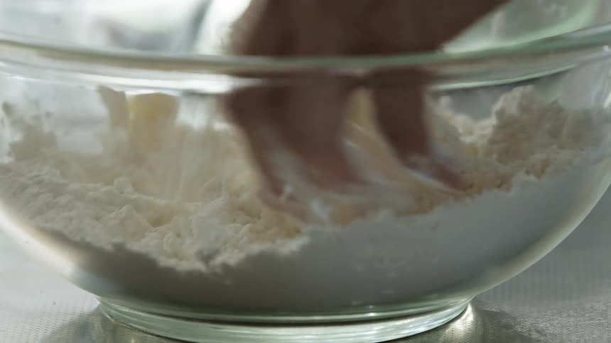 Fingertips mixing flour in a glass bowl