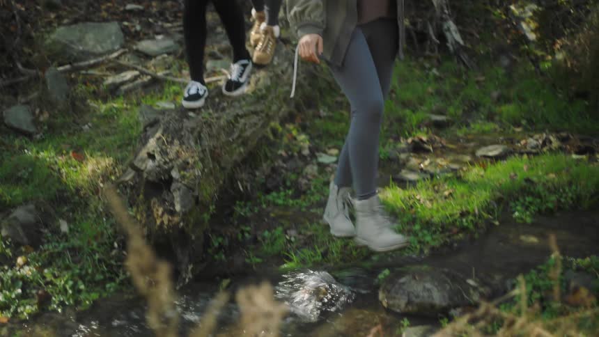 Three female friends walking over the wet rocks of a stream in the forest