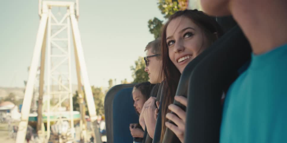Men and women on a amusement park ride with trees the sky and clouds in the background