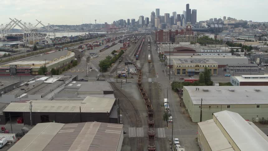 Pullback tilt up reveal of a freight train leaving an urban rail yard with the downtown skyline in the distance