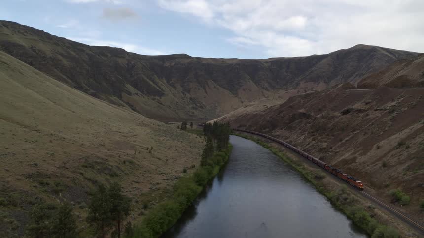 Pullback traverse of a long train traveling next to a river surrounded by hills