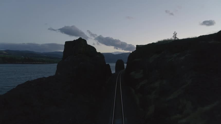 Descent along a length of empty train track reflecting the light of the evening sky