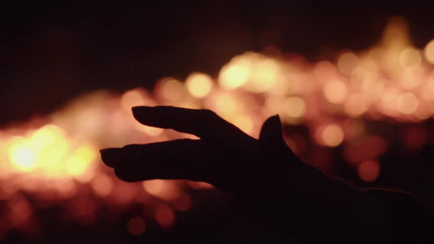 A persons hand in the dark with fire smoke and embers in the background