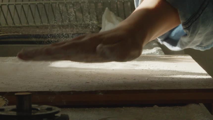 A woman at home dusts flour on a wooden board