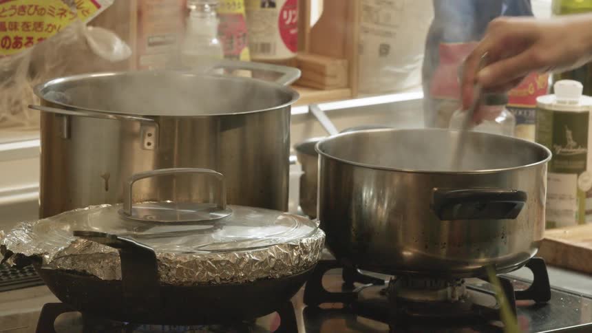 A person with a spoon stirring a pot on a stove in the kitchen