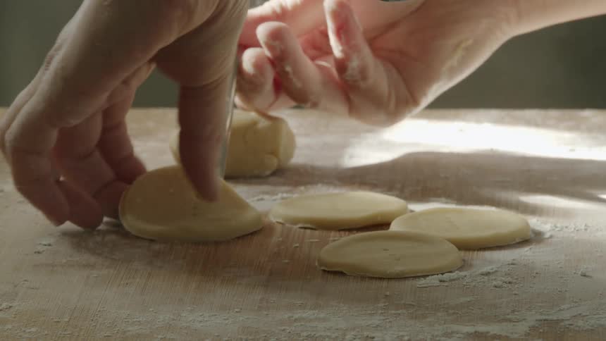 A person uses the back of a fork to peel dough from a wooden surface covered in flour