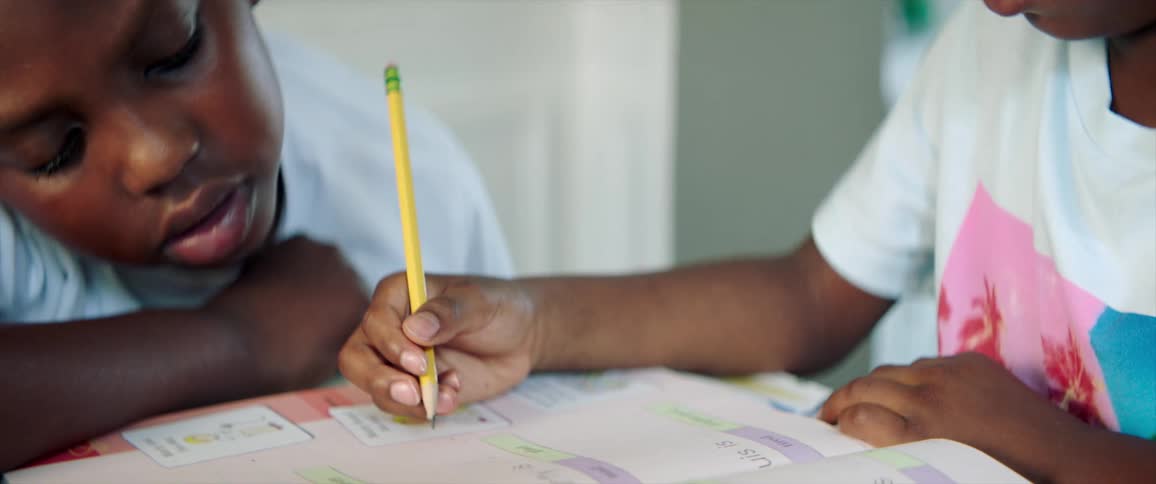 A little boy watches his sister do school work at home