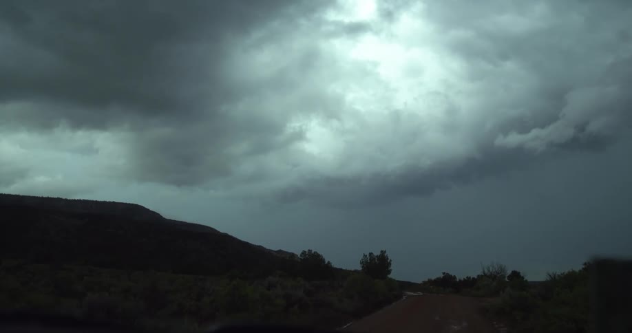 A vehicle with windshield wipers driving on a road with trees the sky and clouds in the background