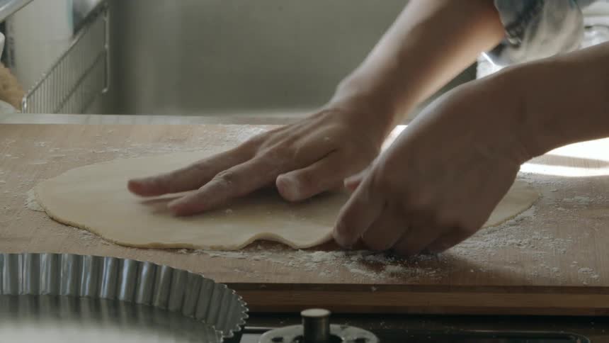 A woman at home flattens dough