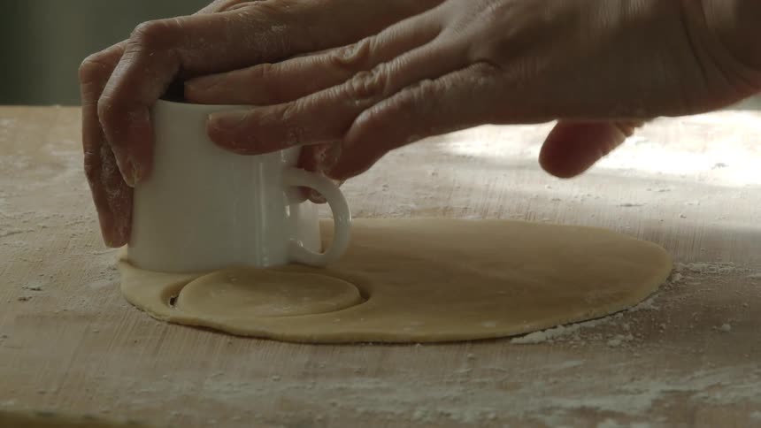 Person uses coffee cup to cut out circles from rolled out dough