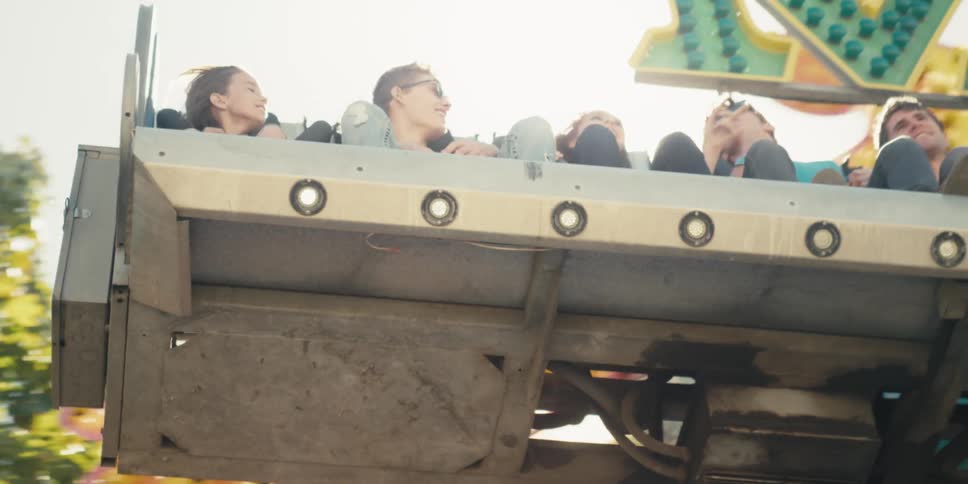 Men and women on an amusement park ride with trees the sky and clouds in the background