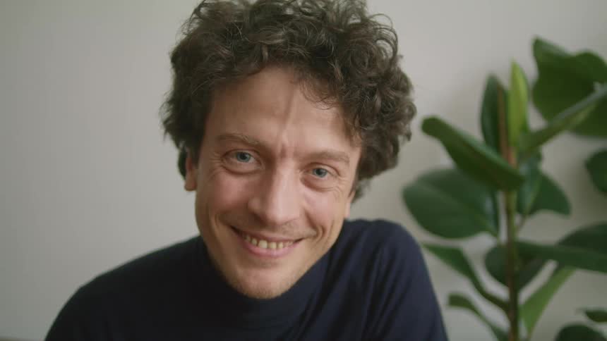 A curly haired man with a big smile indoors