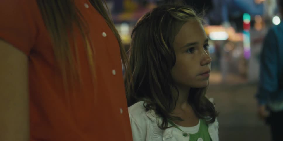 Young blonde girl standing in an amusement park at night
