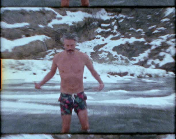 Man sitting on the cold freezing waters of a lake waves at the camera while standing up