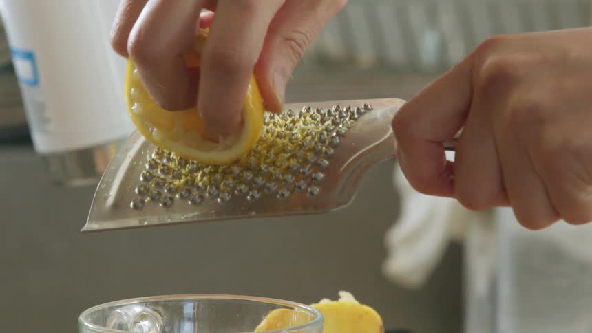 A person grates the rind from a lemon into a glass
