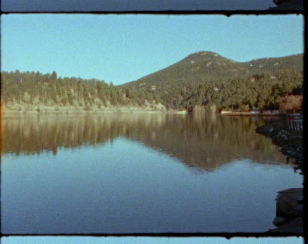 Rippling water reflects forest mountains and clear blue sky