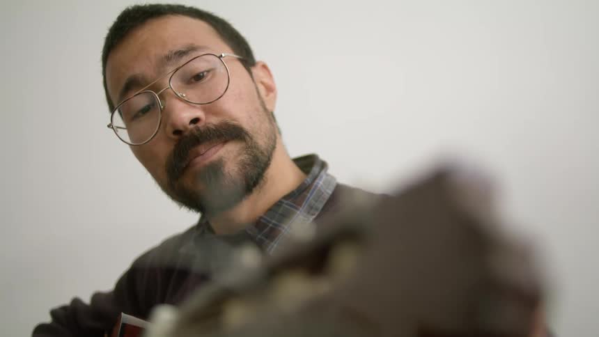 A man holds a guitar and tunes it indoors
