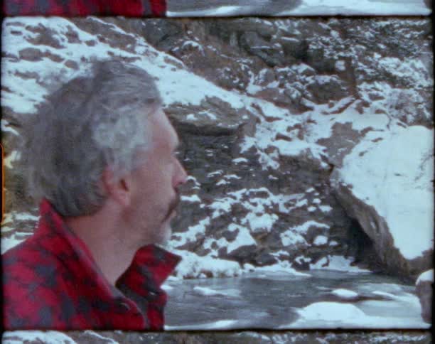 Man with plaid shirt looks around next to the river in the mountainous area