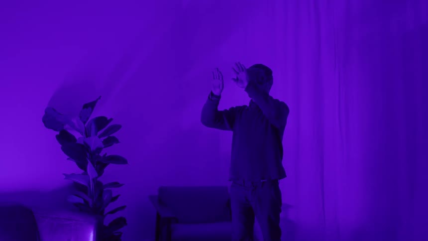 Man wearing virtual reality goggles gesticulates in the air inside a room flooded with magenta lights