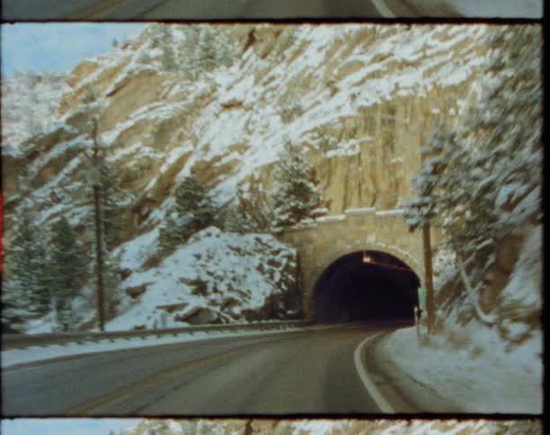 Vehicle driving on a road through the pine tree covered mountains at winters goes in and out of a tunnel