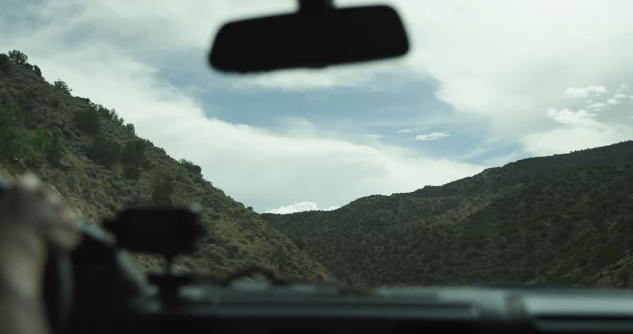A person driving a vehicle on a road with hills the sky and clouds in the background