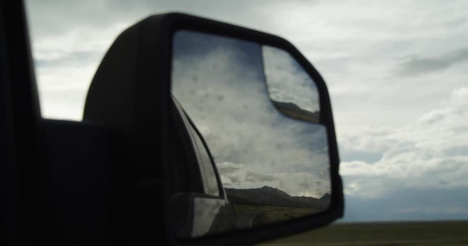 A vehicle with a rearview mirror with the reflection of a mountain range the sky and clouds