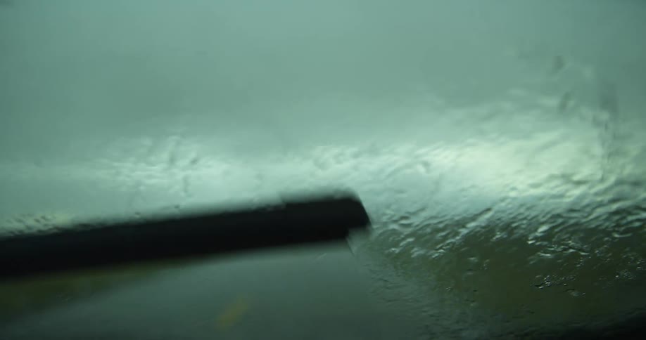 Windshield wipers moving across a windshield as rain falls