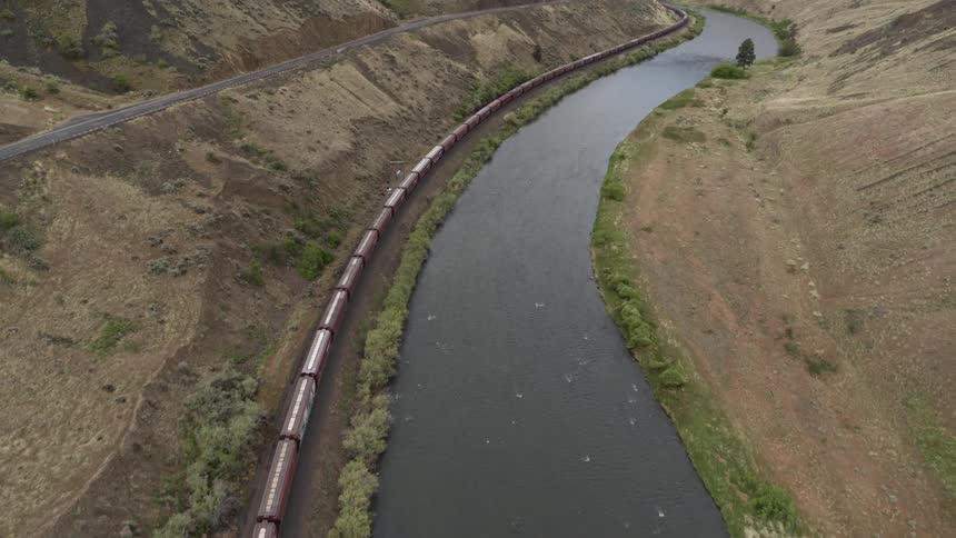 Overhead tilt up of a train traveling along the side of a river