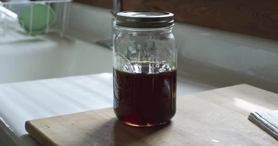 A jar of honey in the kitchen next to a sink and faucet